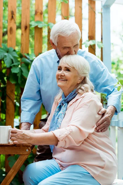 Senior man with closed eyes kissing cheerful wife with grey hair — Stock Photo