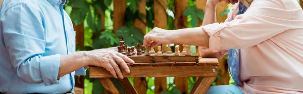 Plano panorámico de pareja jubilada jugando ajedrez en mesa de madera - foto de stock