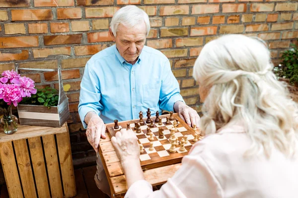 Selective focus of retired man playing chess with senior wife — Stock Photo