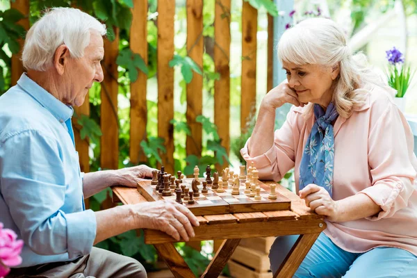 Mujer jubilada con el pelo gris jugando ajedrez con el hombre mayor - foto de stock