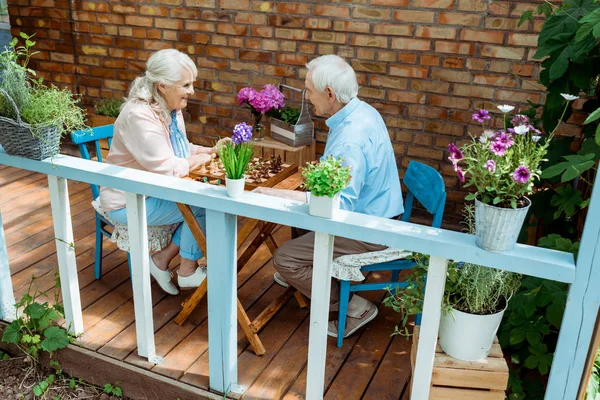 Heureux couple retraité jouant aux échecs tout en étant assis sur la terrasse — Photo de stock