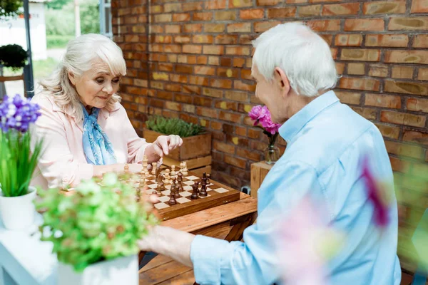 Foco seletivo do homem e da mulher aposentados jogando xadrez — Fotografia de Stock