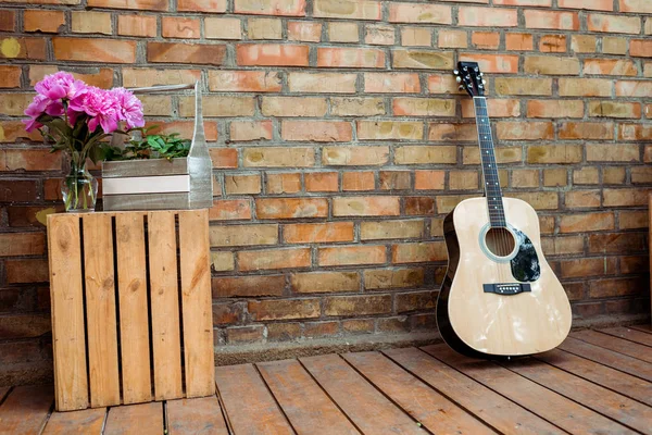 Розовые пионы в вазе возле акустической гитары и кирпичной стены — стоковое фото