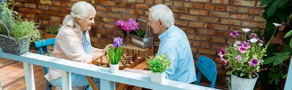 Panoramic shot of happy retired couple playing chess — Stock Photo