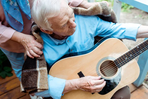 Ausgeschnittene Ansicht einer Seniorin in der Nähe ihres Ehemannes, die Akustikgitarre spielt — Stockfoto
