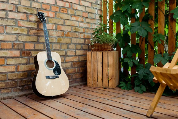 Selective focus of acoustic guitar near brick wall and wooden fence with green leaves — Stock Photo