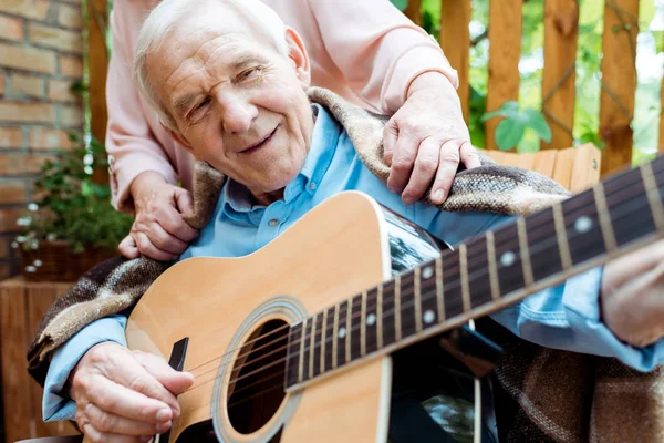 Ausgeschnittene Ansicht einer Seniorin in der Nähe eines glücklichen Ehemannes, der Akustikgitarre spielt — Stockfoto
