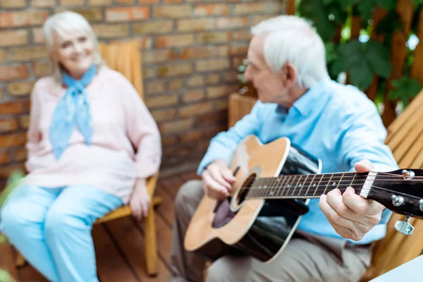 Foco seletivo do marido aposentado tocando guitarra acústica perto da esposa — Fotografia de Stock