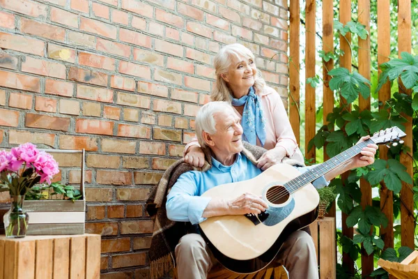 Vue à angle bas du mari à la retraite jouant de la guitare acoustique près de femme heureuse — Photo de stock