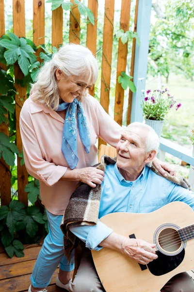 Alegre aposentado marido tocando guitarra acústica perto feliz esposa — Fotografia de Stock