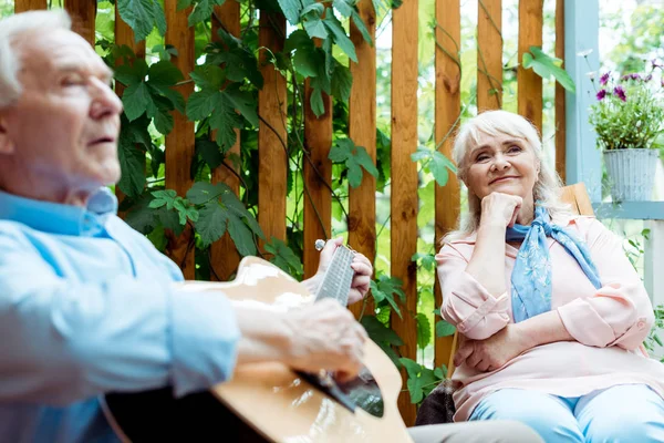 Foco seletivo da mulher aposentada ouvindo enquanto o marido toca guitarra acústica — Fotografia de Stock