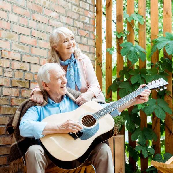 Heureux retraité mari jouer guitare acoustique près de senior femme — Photo de stock