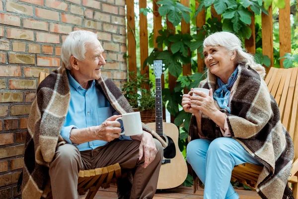 Happy senior man looking at cheerful wife holding cup with tea — Stock Photo