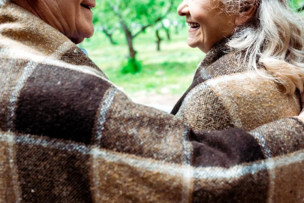 Cropped view of senior husband near happy retired wife in plaid blanket — Stock Photo