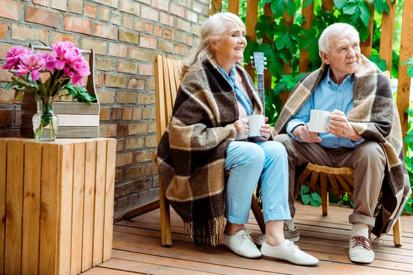 Fröhliche Seniorin und Mann sitzen auf Terrasse und halten Tassen in der Hand — Stockfoto