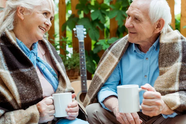 Selective focus of happy senior woman and man looking at each other and holding cups — Stock Photo