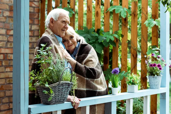 Enfoque selectivo de la mujer mayor feliz en manta a cuadros con el marido en la terraza - foto de stock