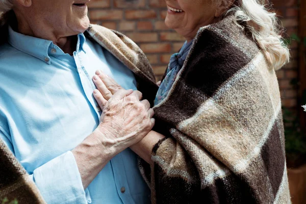 Cropped view of happy retired woman touching senior husband in plaid blanket — Stock Photo