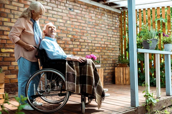 Selective focus of cheerful senior woman standing near disabled husband in wheelchair — Stock Photo