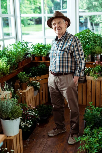 Cheerful senior man standing in straw hat with hands in pockets — Stock Photo