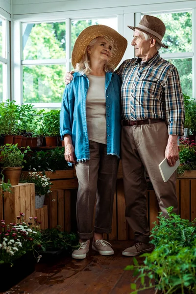 Foco seletivo de homem idoso feliz segurando notebook e olhando para a esposa — Fotografia de Stock