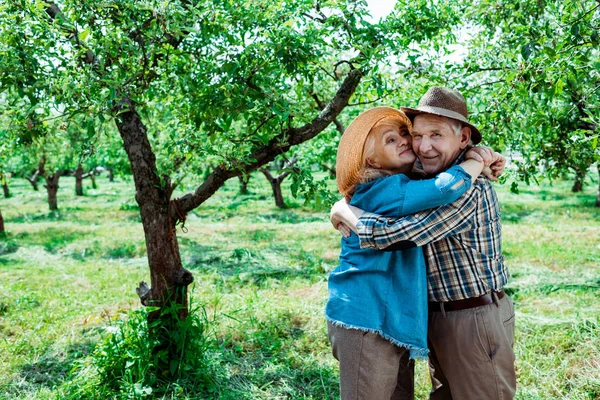 Cheerful senior woman hugging happy retired husband in straw hat — Stock Photo