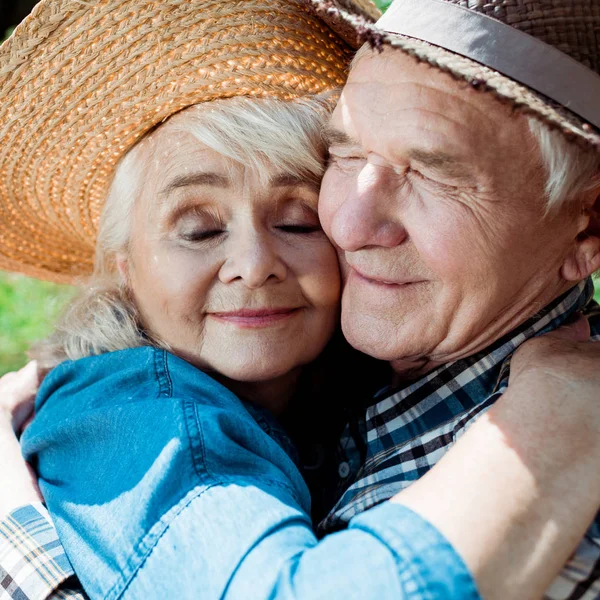 Close up of cheerful senior woman hugging happy retired husband in straw hat — Stock Photo
