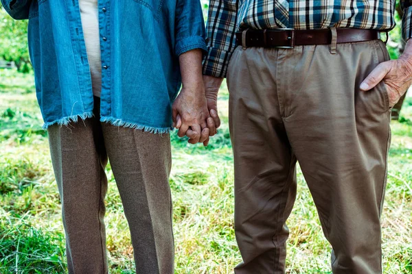 Cropped view of retired woman holding hands with husband standing with hand in pocket — Stock Photo