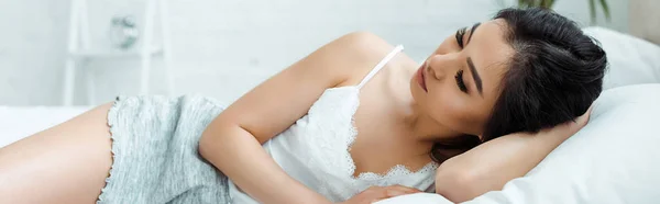 Panoramic shot of attractive asian girl lying on bed with closed eyes — Stock Photo
