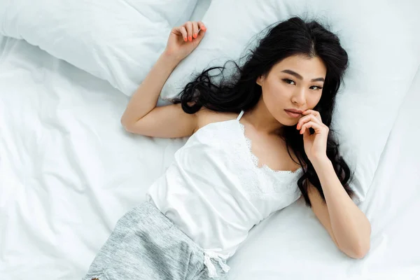 Overhead view of attractive thai woman looking at camera while lying in bedroom — Stock Photo