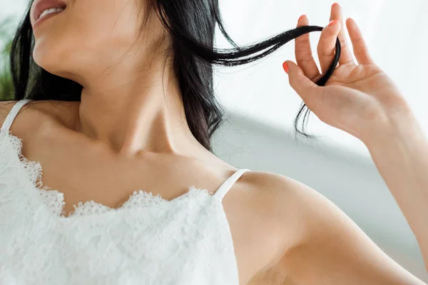 Обрізаний вид щасливої брюнетки жінка торкається волосся вдома — стокове фото