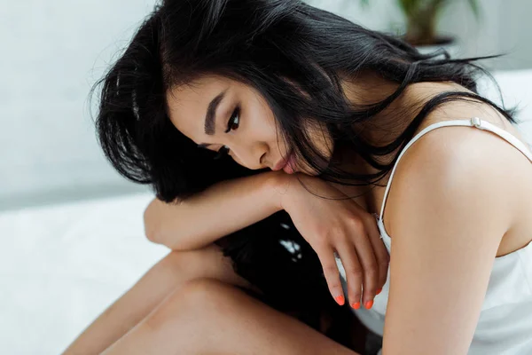 Schöne und verärgerte thailändische Frau sitzt zu Hause auf dem Bett — Stockfoto