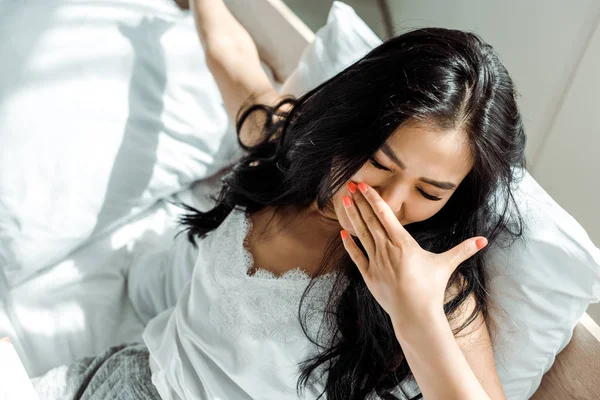 Overhead view of asian woman with closed eyes covering face with yawning — Stock Photo