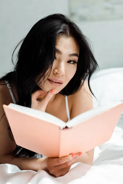 Foco seletivo de mulher tailandesa bonita segurando livro e olhando para a câmera — Fotografia de Stock