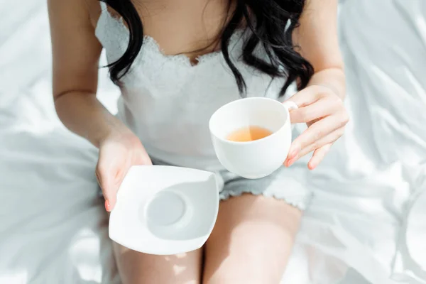 Вид зверху брюнетка жінка тримає чашку з чаєм в спальні — стокове фото
