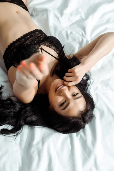 Enfoque selectivo de la mujer tailandesa feliz en ropa interior negro acostado en la cama - foto de stock