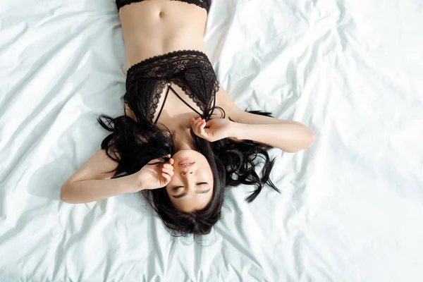 Vue de dessus de la femme thai avec les yeux fermés en noir sous-vêtements sexy couché sur le lit — Photo de stock