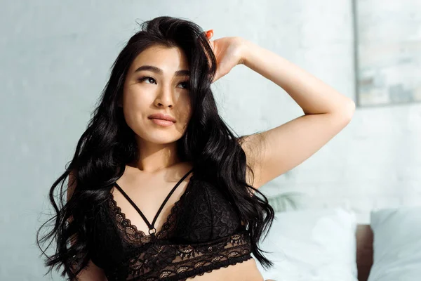 Чуттєва тайська жінка в сексуальному мереживному бюстгальтері торкається волосся в спальні — стокове фото