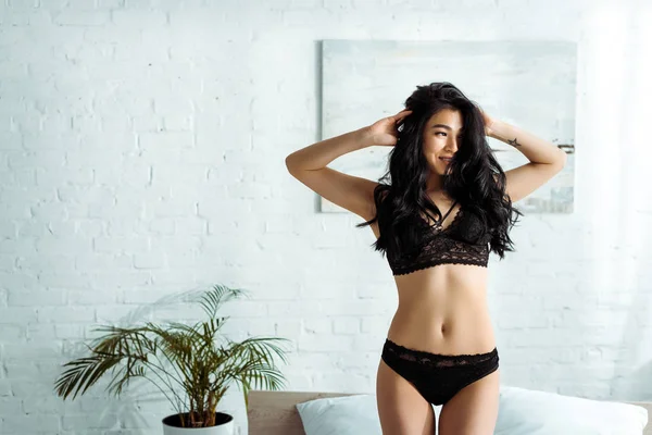 Happy asian young woman in lace underwear standing and touching hair — Stock Photo