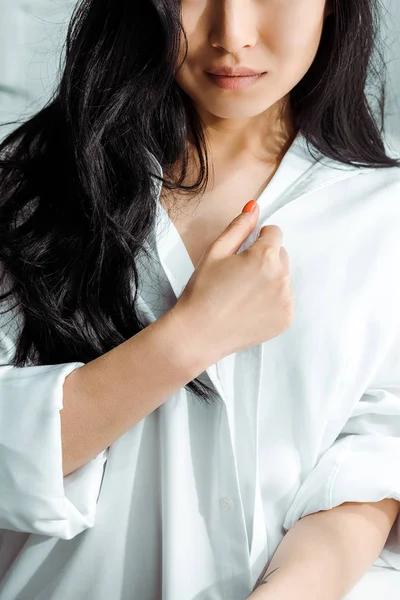 Cropped view of brunette young woman touching white shirt — Stock Photo