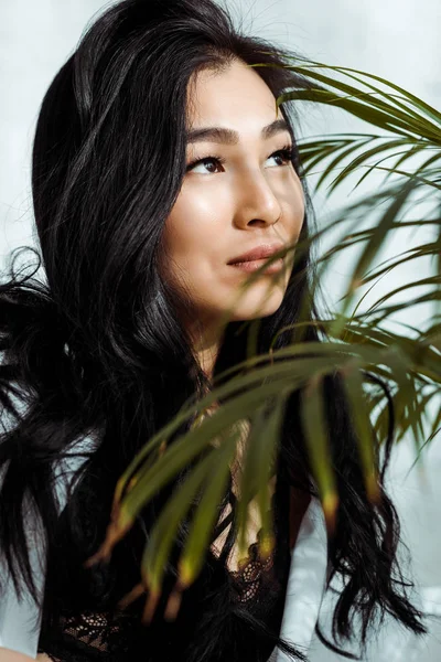 Селективный фокус привлекательной азиатской женщины вблизи зеленого растения — стоковое фото