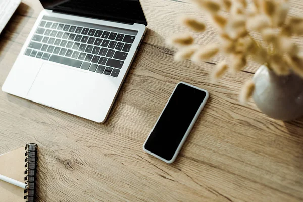 Enfoque selectivo de teléfono inteligente con pantalla en blanco cerca de la computadora portátil - foto de stock