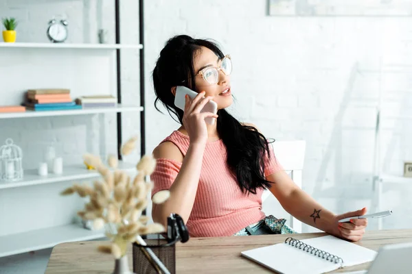 Selektiver Fokus attraktiver asiatischer Geschäftsfrau in Brille, die im Büro mit Smartphone spricht — Stockfoto