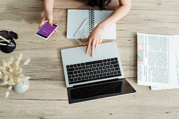 KYIV, UCRANIA - 23 de mayo de 2019: vista recortada de una mujer joven usando una computadora portátil con pantalla en blanco y un teléfono inteligente con aplicación instagram - foto de stock