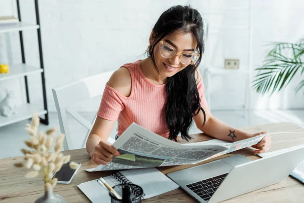 Enfoque selectivo de alegre asiático mujer en gafas lectura periódico en oficina - foto de stock