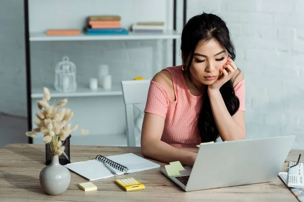 Attractive asian girl using laptop near notebook in office — Stock Photo