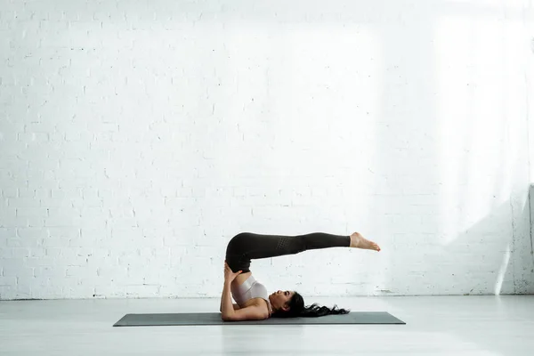 Hermosa asiático mujer haciendo ejercicio en yoga mat cerca de ladrillo pared - foto de stock