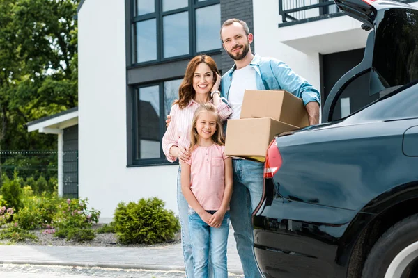 Cheerful man holding boxes near happy wife and daughter — Stock Photo