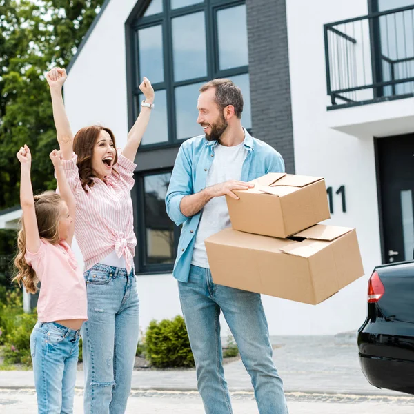 Happy woman and kid gesturing near cheerful bearded man with boxes — Stock Photo