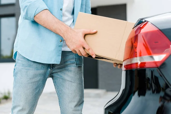 Vista cortada do homem colocando caixa de papelão no carro moderno — Fotografia de Stock